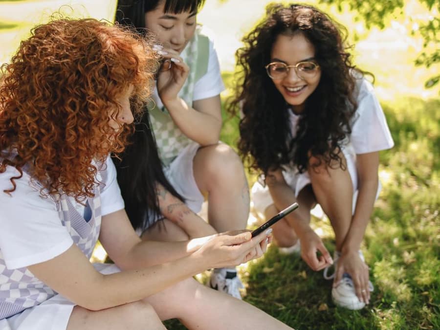 Three friends outdoors smiling at a phone using WAYA